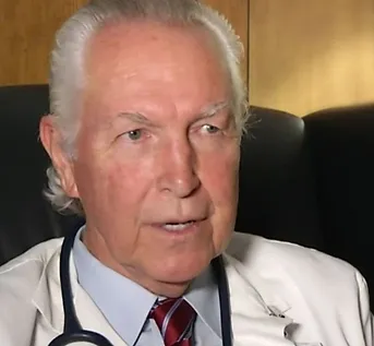 Dr. Harold Potts in a chair wearing a white doctor's coat and stethoscope around his neck